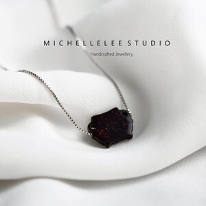 May include: A silver chain necklace with a red and black geometric pendant. The pendant has a sparkly, glittery finish. The text "MICHELLELEE STUDIO" and "Handcrafted Jewellery" is visible in the background.