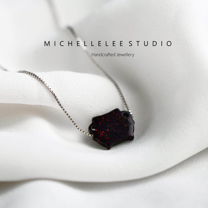 May include: A silver chain necklace with a red and black geometric pendant. The pendant has a sparkly, glittery finish. The text "MICHELLELEE STUDIO" and "Handcrafted Jewellery" is visible in the background.