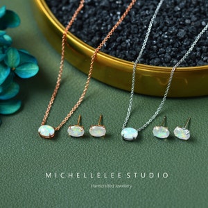 May include: A set of opal jewelry featuring a necklace and earrings. The necklace is available in both rose gold and silver, and the earrings are silver. The opal stones are oval-shaped and have a white iridescent color.