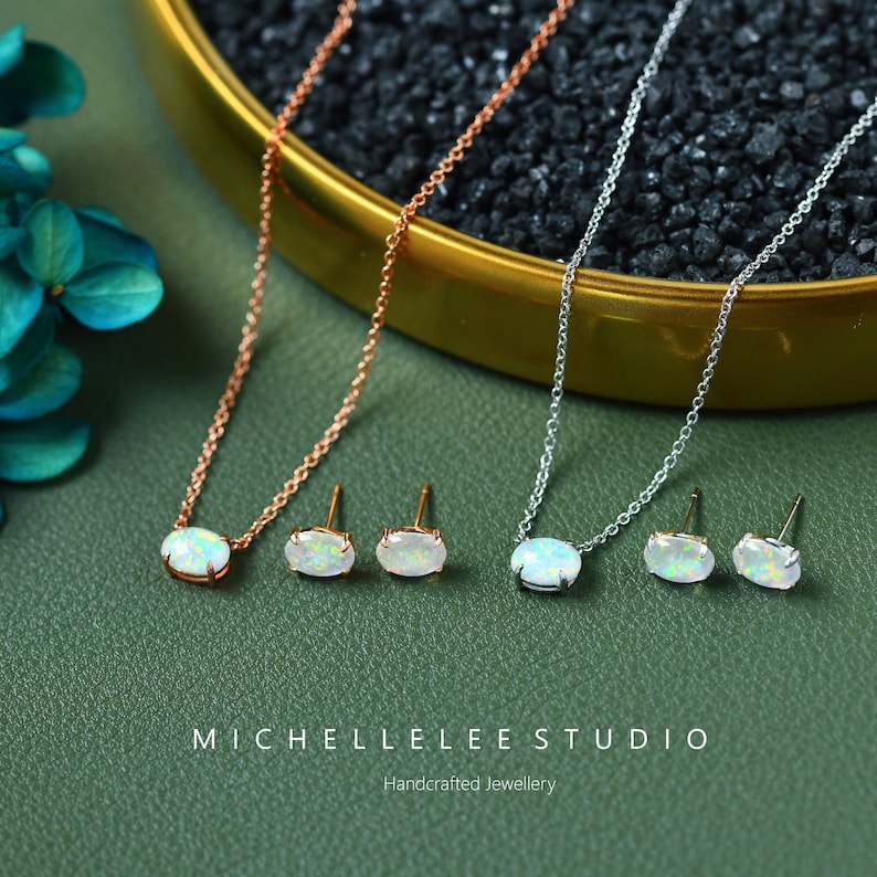May include: A set of opal jewelry featuring a necklace and earrings. The necklace is available in both rose gold and silver, and the earrings are silver. The opal stones are oval-shaped and have a white iridescent color.