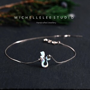 Puede incluir: Una delicada pulsera de plata con un dije de caballito de mar con colores iridiscentes tipo &oacute;palo. La pulsera tiene una fina cadena y peque&ntilde;as cuentas de plata. El texto "MICHELLELEE STUDIO Handcrafted Jewellery" es visible.