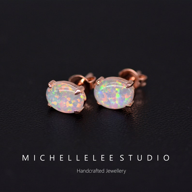 May include: A pair of oval-shaped opal earrings with a rose gold setting. The earrings are on a black surface.