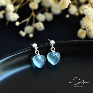 May include: A pair of silver heart-shaped earrings with light blue gemstone drops. The earrings are on a black surface.