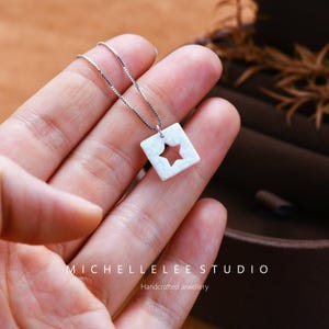 May include: A silver chain necklace with a white opal pendant featuring a star cut-out. The pendant is square shaped and has a delicate, minimalist design.  Handcrafted Jewellery.