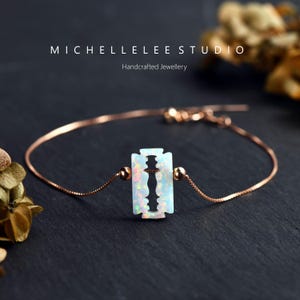 Könnte beinhalten: Ein zartes Armband aus roségoldener Kette mit einem weißen Opal-Rasiermesser-Anhänger. Der Anhänger ist ein einzigartiges und kantiges Schmuckstück.