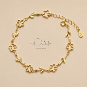 May include: A gold bracelet with a floral design and white detailing. The bracelet features flower-shaped charms and leaf accents, connected by a delicate chain. The brand name "mi Chellelee" is displayed in the image.