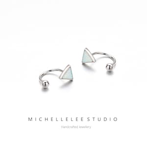 May include: A pair of silver hoop earrings with a small triangle-shaped opal stone on each hoop. The earrings are designed to be worn in the upper ear cartilage.