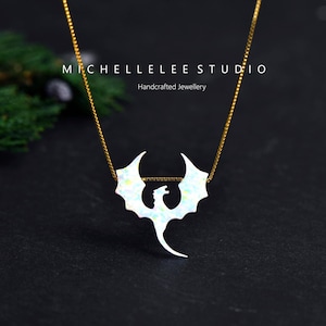 May include: A gold chain necklace featuring a white dragon pendant. The dragon pendant has a wing span design and is made of a pearlescent material. The text "MICHELLELEE STUDIO Handcrafted Jewellery" is at the top.