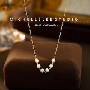 May include: A gold necklace with a series of small, round, white gemstones. The necklace is displayed on a brown velvet surface. The text "MICHELLELEE STUDIO Handcrafted Jewellery" is visible.