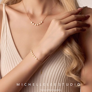 May include: A gold necklace and bracelet set featuring a series of small, white pearls. The necklace is a delicate design, and the bracelet is adjustable. The image also displays the text "MICHELLELEE STUDIO Handcrafted Jewellery".