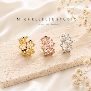 May include: Three flower-shaped earrings in gold, rose gold, and silver. The earrings are displayed on a light-colored surface with the text "MICHELLELEE STUDIO Handcrafted Jewellery". The earrings are a floral design.