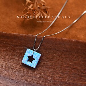 May include: A silver chain necklace with a blue opal pendant featuring a star cutout. The pendant is square shaped and has a light blue color with iridescent flecks. The text "MICHELLELEE STUDIO Handcrafted Jewellery" is visible in the background.