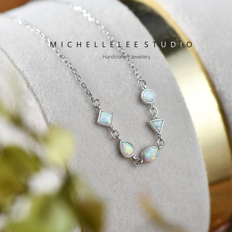 May include: A silver chain necklace with five opal stones in different shapes, including a circle, a square, a triangle, and two teardrop shapes. The necklace is on a white background with the text "MICHELLE LEE STUDIO Handcrafted Jewellery".