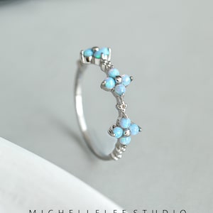 Könnte beinhalten: Ein silberner Ring mit drei blütenförmigen Clustern aus blauen Opalen. Der Ring ist handgefertigt und hat ein zartes Design.