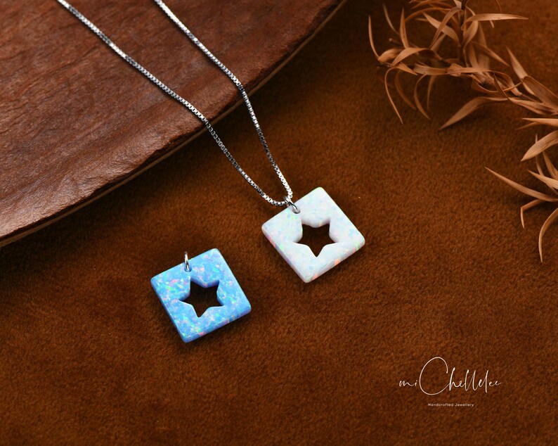 May include: A silver chain necklace with two opal pendants. The pendants are square shaped with a star cut out. One pendant is white opal and the other is blue opal.