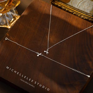 May include: A silver necklace and bracelet set with a delicate scissor charm. The jewelry is displayed on a wooden surface with the text "MICHELLELEE STUDIO Handcrafted Jewellery".