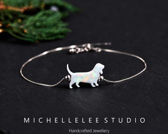 Puede incluir: Una delicada pulsera de cadena plateada con un dije central de perro en estilo ópalo blanco. La figura del perro está flanqueada por dos pequeñas cuentas plateadas en una cadena fina y ajustable. Se lee el texto MICHELLELEE STUDIO Handcrafted Jewellery.