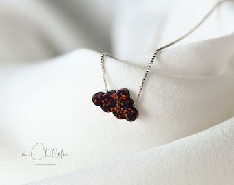 Puede incluir: Un collar de cadena de plata con un colgante en forma de nube hecho de ópalo negro iridiscente. El colgante tiene un aspecto moteado y multicolor.