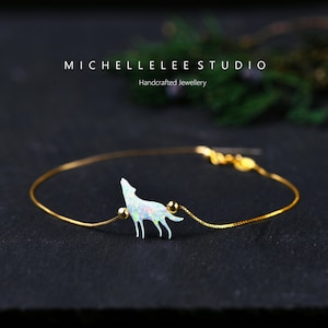 May include: A delicate gold-toned bracelet featuring a howling wolf pendant with an iridescent, opal-like finish. The bracelet has a fine chain and small gold beads. The brand name "MICHELLELEE STUDIO" is displayed above the product.