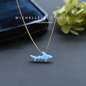 May include: A delicate gold chain necklace with a blue opal shark pendant. The pendant is a simple, minimalist design and is perfect for everyday wear.