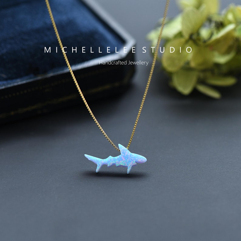 May include: A delicate gold chain necklace with a blue opal shark pendant. The pendant is a simple, minimalist design and is perfect for everyday wear.