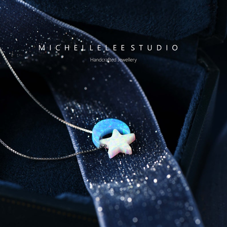 May include: A silver chain necklace with a blue and white opal crescent moon and star pendant. The pendant is in a velvet box with the text "MICHELLE LEE STUDIO Handcrafted Jewellery".