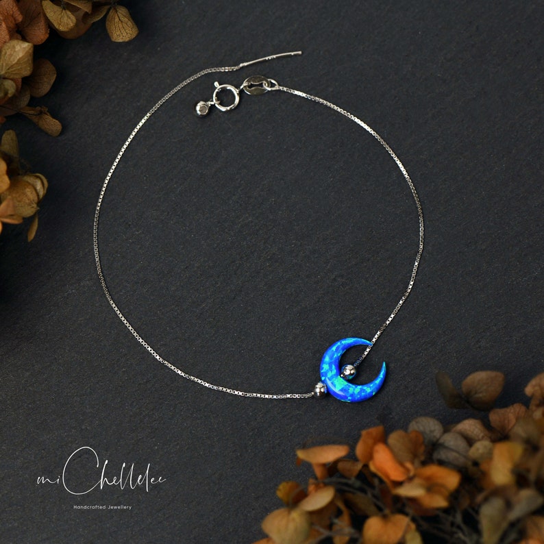 May include: A delicate silver chain anklet with a crescent moon charm featuring a blue opal stone.