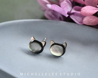May include: A pair of silver stud earrings featuring a black cat design made from mother of pearl.