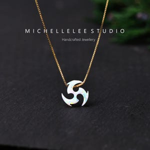May include: A gold-colored necklace with a pendant in the shape of a stylized spiral. The pendant is white with iridescent accents. The necklace is displayed on a dark surface. Text on the image reads "MICHELLELEELEE STUDIO Handcrafted Jewellery."