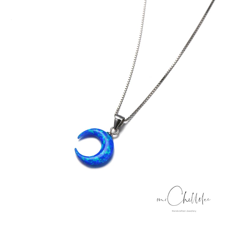 K&ouml;nnte beinhalten: Eine silberne Kettenkette mit einem Halbmond-Anh&auml;nger aus blauem Opal. Der Anh&auml;nger hat eine glitzernde, irisierende Oberfl&auml;che.