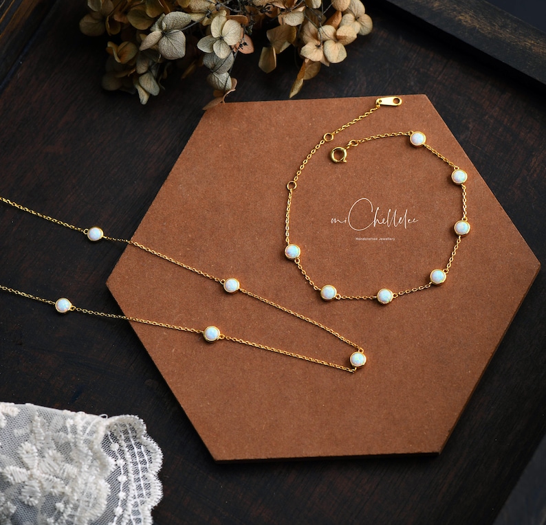 Pode incluir: Um conjunto de colar e pulseira dourados com pequenas pedras brancas redondas. As joias s&atilde;o exibidas em uma superf&iacute;cie hexagonal marrom, com flores secas ao fundo. A marca "mr. Chellelee" &eacute; vis&iacute;vel.