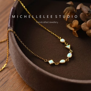 May include: A gold chain necklace with white opal stones in various shapes, including ovals, squares, and triangles. The necklace is displayed in a brown velvet box with the text "MICHELLE LEE STUDIO Handcrafted Jewellery".