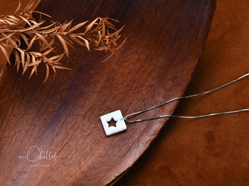 May include: A silver chain necklace with a white ceramic pendant featuring a star cutout. The pendant is on a brown wooden surface.