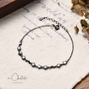 Puede incluir: Un delicado brazalete de cadena negra con pequeñas piedras de ópalo blanco y abalorios de estrella y media luna.