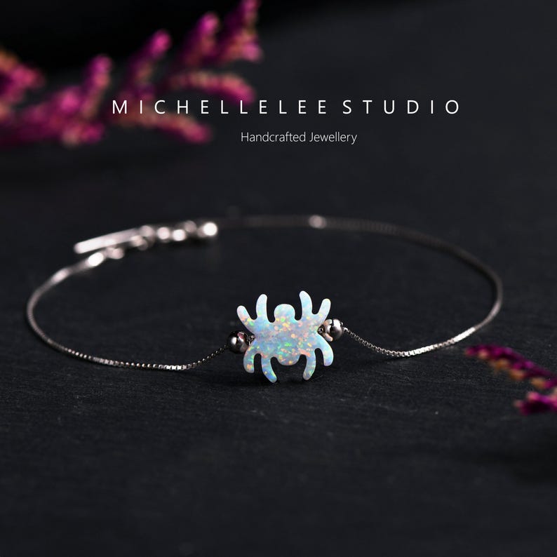 May include: A silver chain bracelet with a white opal spider charm. The bracelet is on a black background.