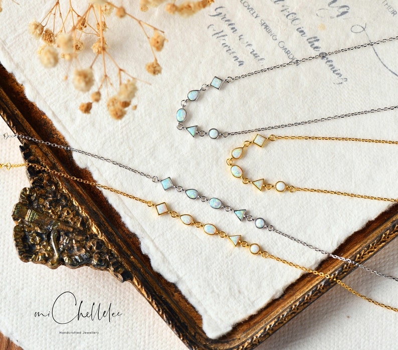 May include: Three delicate necklaces with opal stones and silver and gold chains. The necklaces are arranged on a white textured surface with the text "an Chellelee Handcrafted Jewellery".