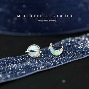 May include: A pair of silver earrings with opal stones. One earring is a crescent moon shape and the other is a circle with a silver band around it, representing a planet.