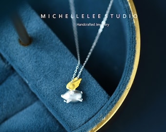 May include: A silver necklace with a small pig charm with gold wings. The necklace is displayed in a blue velvet jewelry box with the text "MICHELLELEE STUDIO Handcrafted Jewelry" on the top.