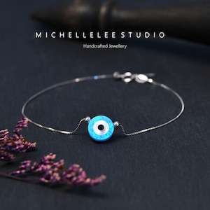 Può includere: Un braccialetto a catena d'argento con un ciondolo blu e bianco di occhio turco. Il ciondolo è fatto di opale e ha una pupilla nera. Il braccialetto è fatto a mano ed è un simbolo popolare di protezione.