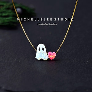 May include: A gold chain necklace featuring a white iridescent ghost pendant and a small pink heart-shaped pendant. The text MICHELLELEE STUDIO Handcrafted Jewellery is visible above the charms. The necklace has a delicate box chain design.