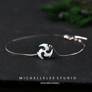 May include: A delicate silver bracelet featuring a stylized, white opal pendant. The pendant has a unique, swirling design. The bracelet is handcrafted and has a simple, elegant style. The text "MICHELLELEE STUDIO" and "Handcrafted Jewellery" are at the bottom.