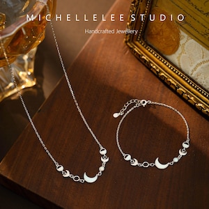 May include: A silver necklace and bracelet set featuring a crescent moon and circle design. The jewelry is displayed on a wooden surface. The text "MICHELLELEE STUDIO Handcrafted Jewellery" is visible in the background.