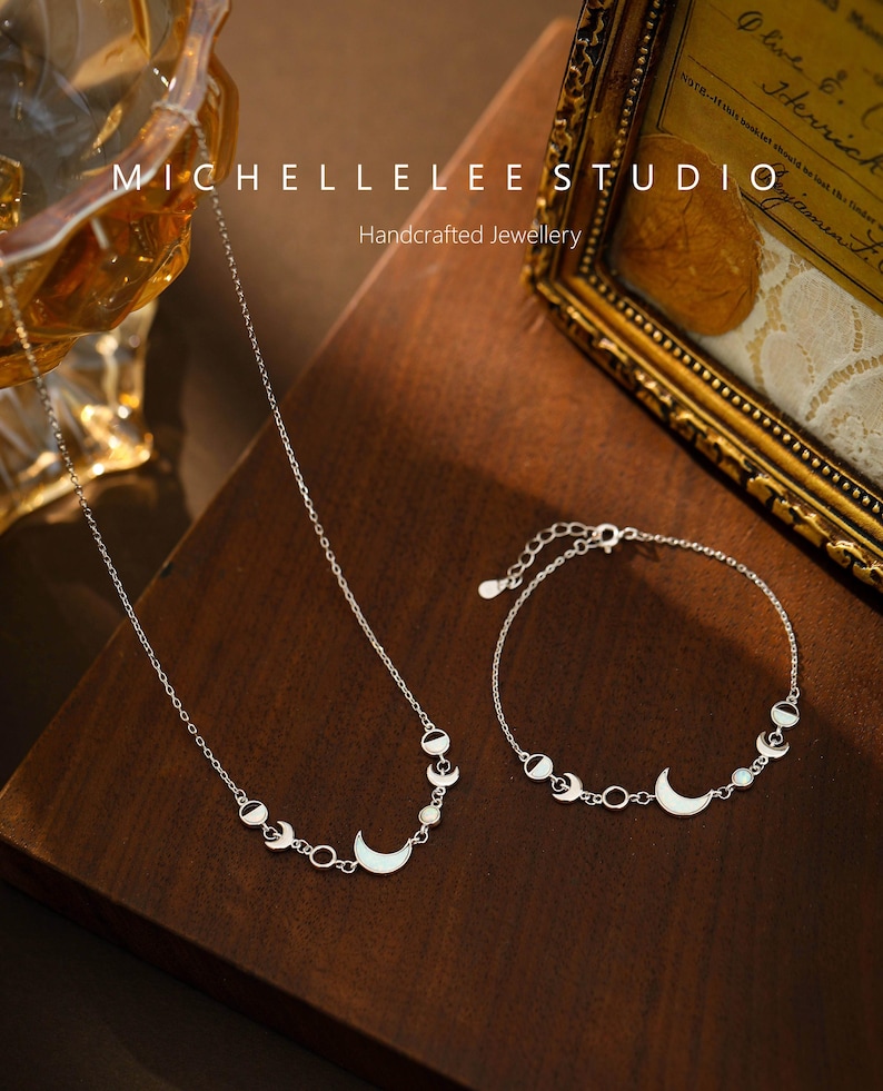 May include: A silver necklace and bracelet set featuring a crescent moon and circle design. The jewelry is displayed on a wooden surface. The text "MICHELLELEE STUDIO Handcrafted Jewellery" is visible in the background.