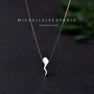 May include: A delicate necklace featuring a thin metal chain and a small, iridescent white opal pendant shaped like a sperm cell. The text MICHELLELEE STUDIO Handcrafted Jewellery is visible in the upper portion of the image.