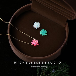 May include: Three clover necklaces with gold chains and opal pendants in pink, white, and green. The necklaces are displayed in a brown jewellery box. The text "MICHELLELEE STUDIO Handcrafted Jewellery" is at the bottom.