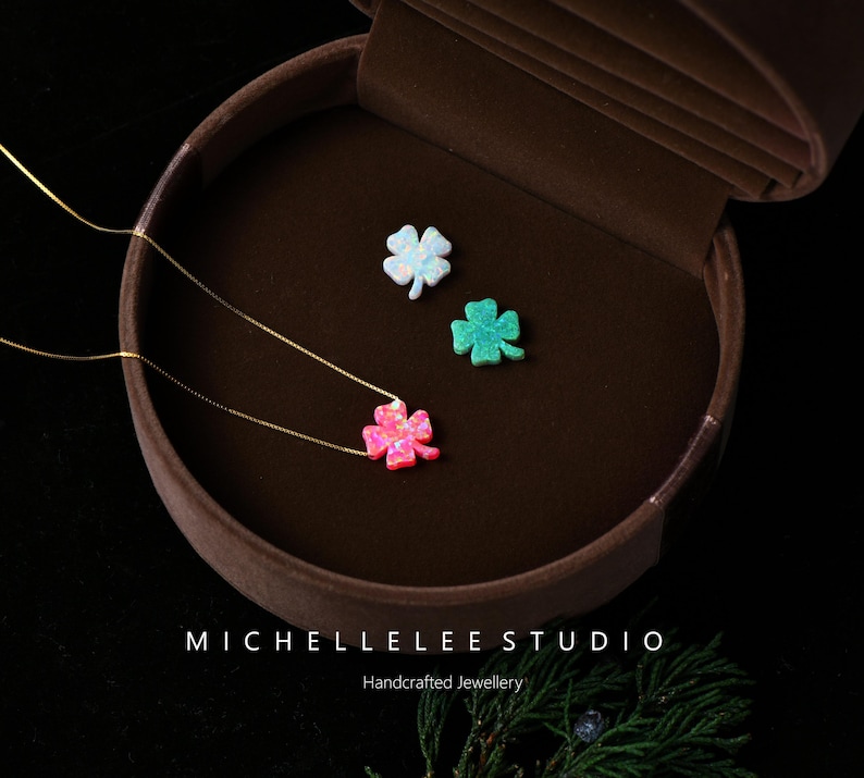 May include: Three clover necklaces with gold chains and opal pendants in pink, white, and green. The necklaces are displayed in a brown jewellery box. The text "MICHELLELEE STUDIO Handcrafted Jewellery" is at the bottom.
