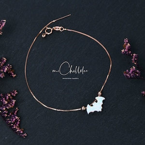 May include: A rose gold chain bracelet featuring a white opal bat-shaped charm flanked by two small rose gold beads. The bracelet includes a spring ring clasp and a thin box chain. The text miChellee Handcrafted Jewellery is centered.