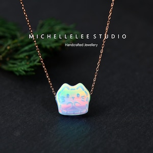 May include: A rose gold chain necklace with a cat pendant. The pendant is iridescent with a cat face design. The necklace is displayed on a dark background with the text "MICHELLELEE STUDIO Handcrafted Jewellery".
