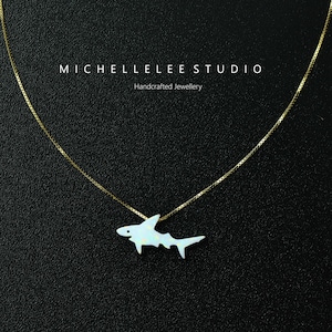 May include: A gold chain necklace with a white opal shark pendant. The pendant is a detailed silhouette of a shark with a white opal stone filling the shape. The necklace is on a black background. "MICHELLELEESTUDIO Handcrafted Jewellery" is written in white text at the top of the image.