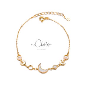 May include: A gold-colored bracelet featuring a crescent moon and circular opal charms. The bracelet has a delicate chain and a lobster clasp closure. The text "mi Chellelee" is visible in the image.